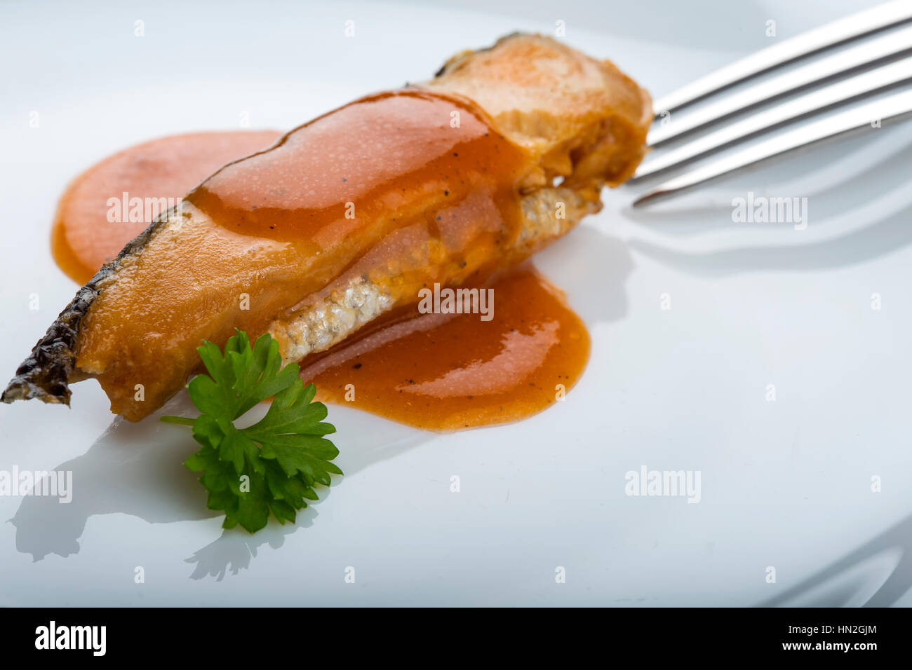 Marinated herring fish in tomato sauce on plate with parsley and fork in background Stock Photo