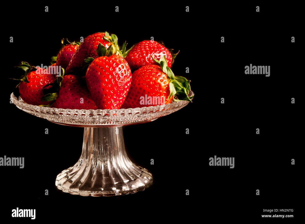 strawberries on a glass stand against black background Stock Photo - Alamy