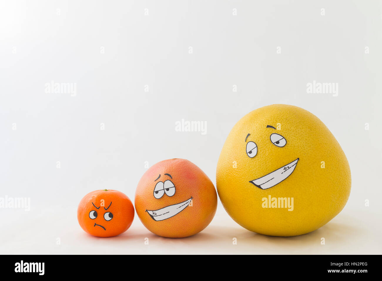 A big yellow honey pomelo with an orange grapefruit and a tangerine with funny faces and white background Stock Photo