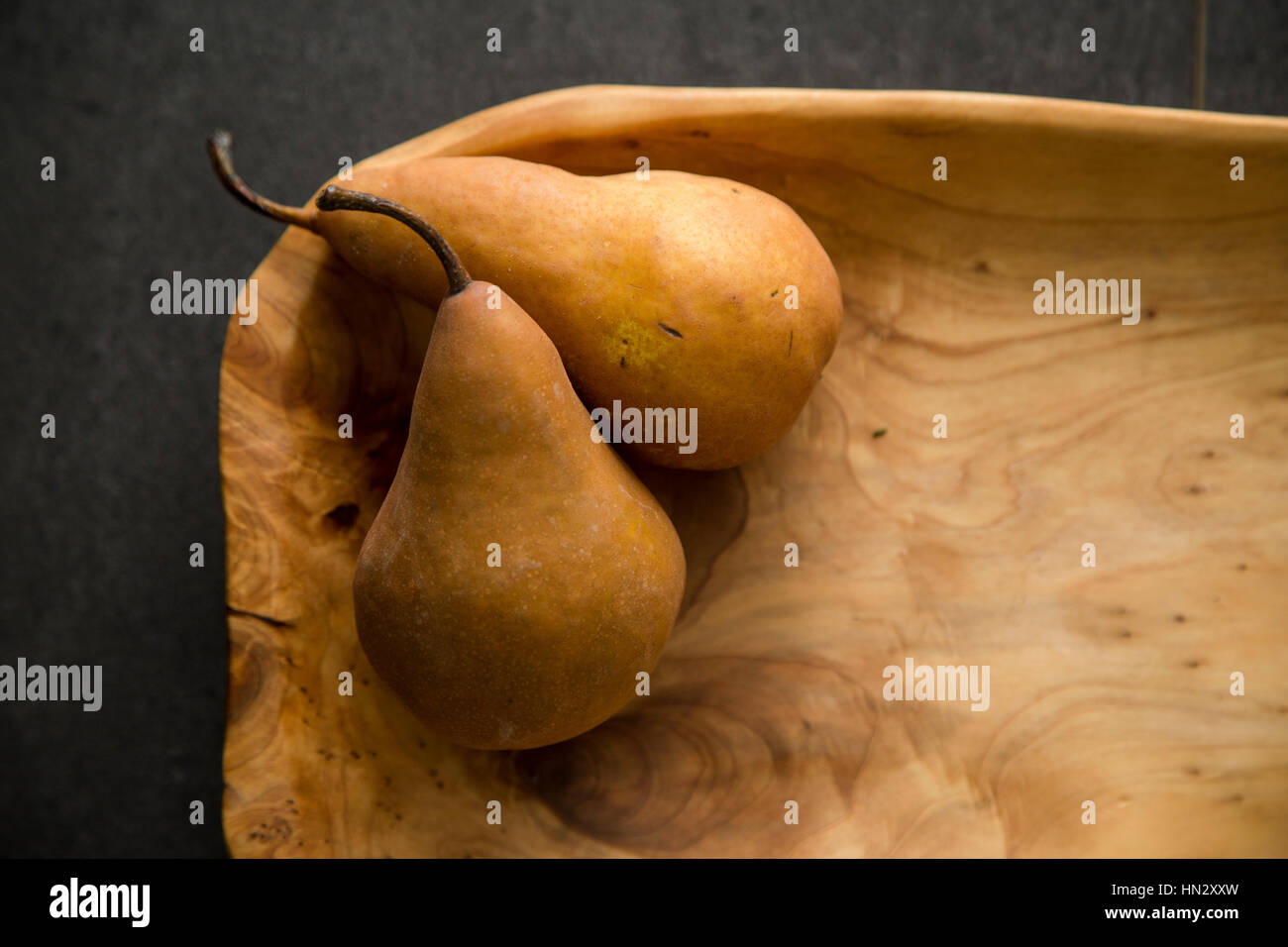Two organic bosc pears in a hand carved wooden platter on a dark table top. Stock Photo