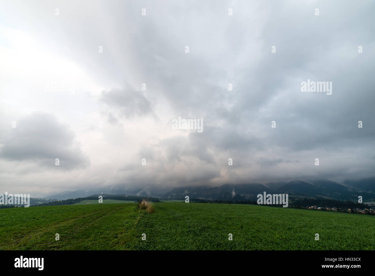 Dark storm clouds over meadow with green grass and mountains in ...
