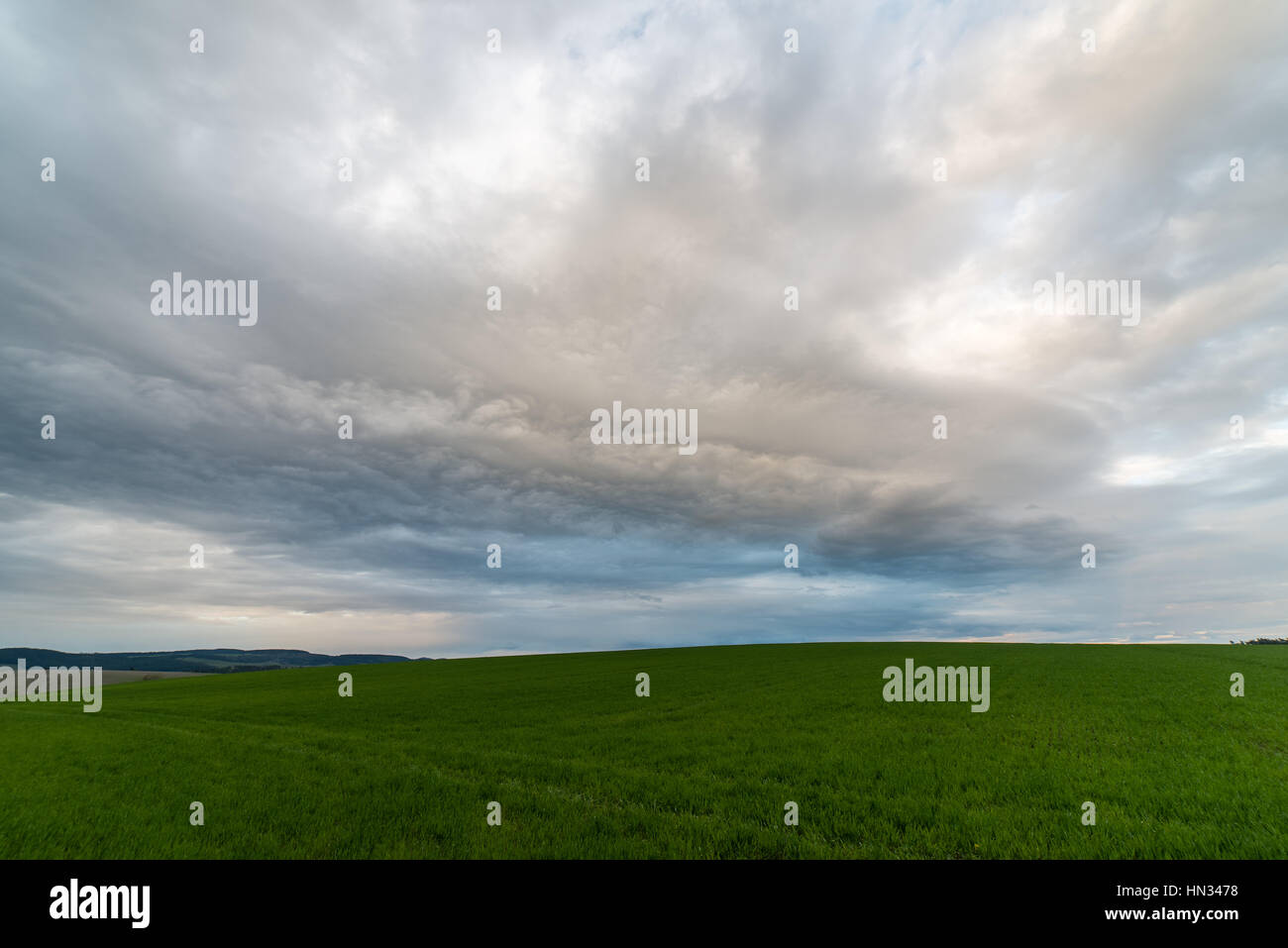 Dark storm clouds over meadow with green grass and mountains in ...