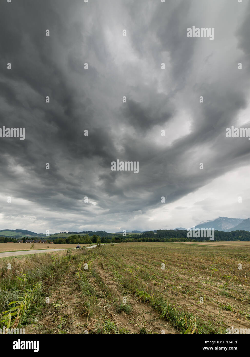 Dark storm clouds over meadow with green grass and mountains in ...
