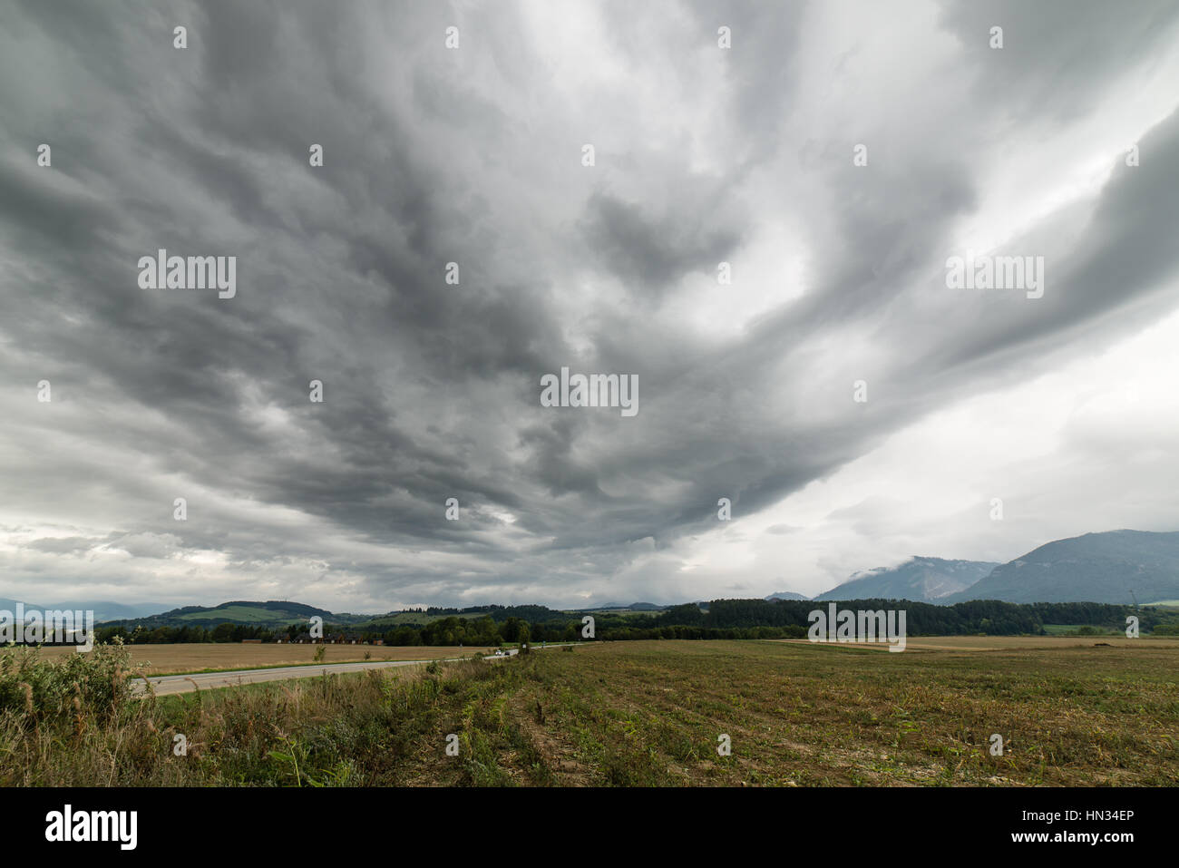 Dark storm clouds over meadow with green grass and mountains in ...