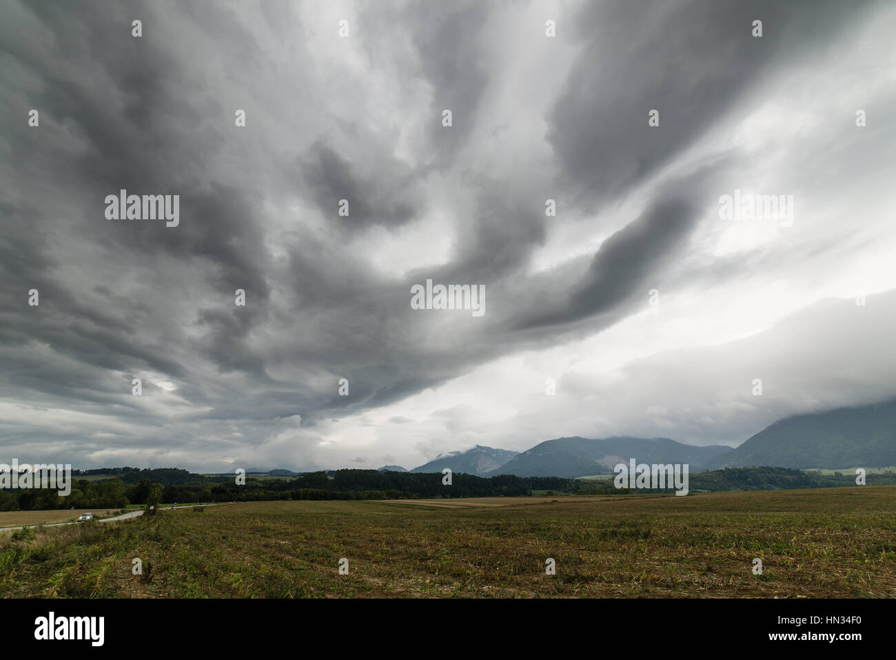 Dark storm clouds over meadow with green grass and mountains in ...