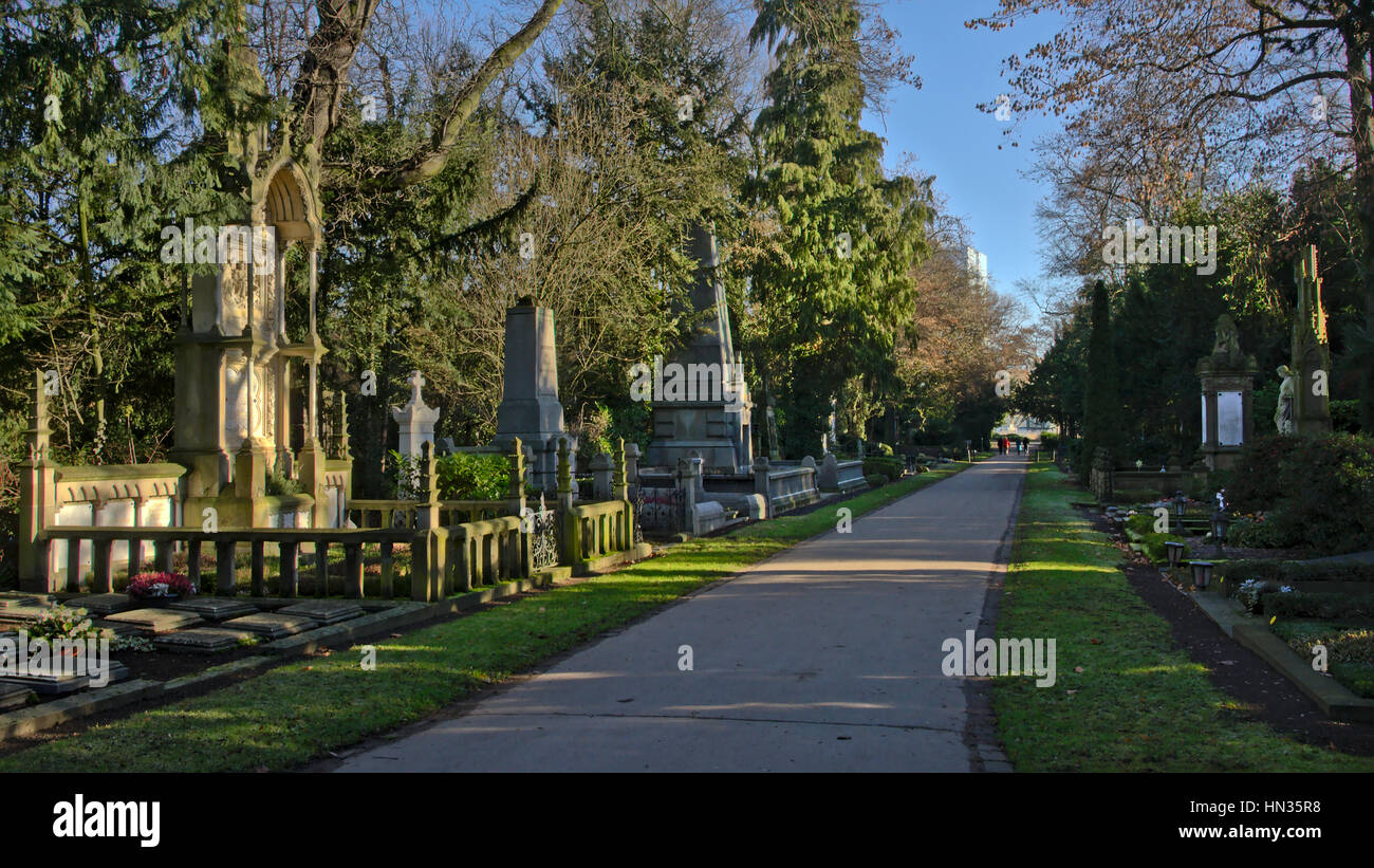 Lane in Melaten cemetery with many old grave monuments in a green environment on a sunny winter day Stock Photo