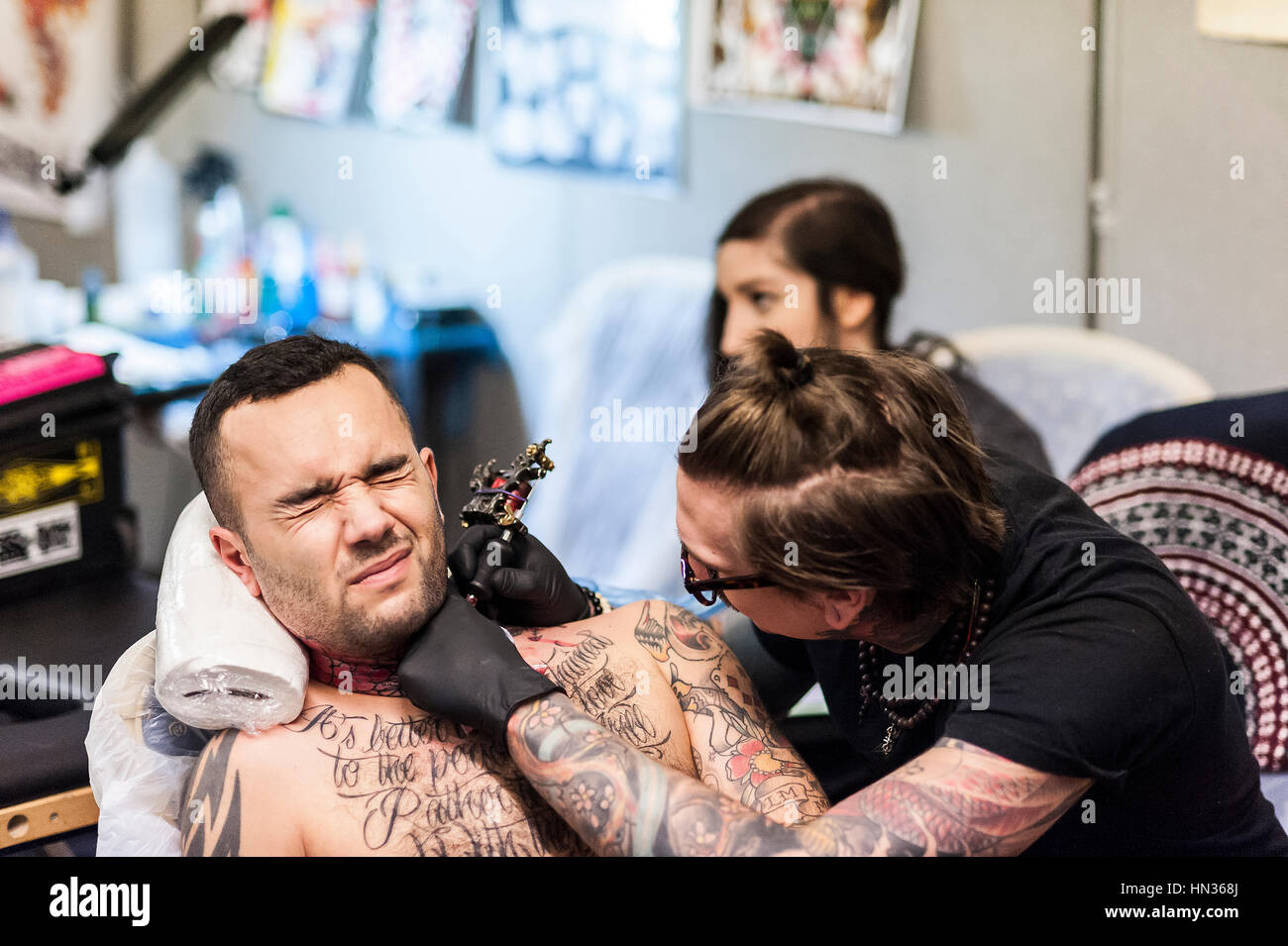 A man endures the pain as he is tattooed on his neck. Stock Photo