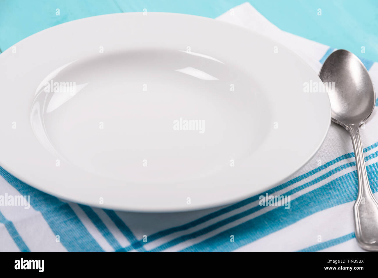 Empty White Plate With Blue Napkin And Spoon On Table Stock Photo