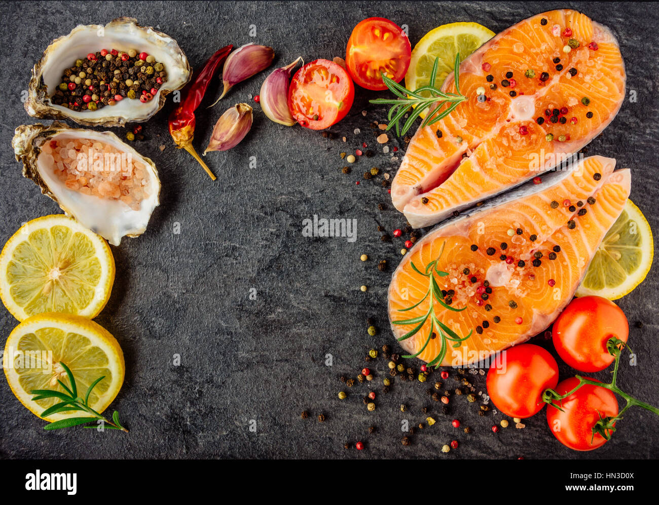 Delicious salmon steak , rich in omega 3 oil, with aromatic herbs and spices with a lemon, tomato, garlic on black background. Healthy and diet food.  Stock Photo