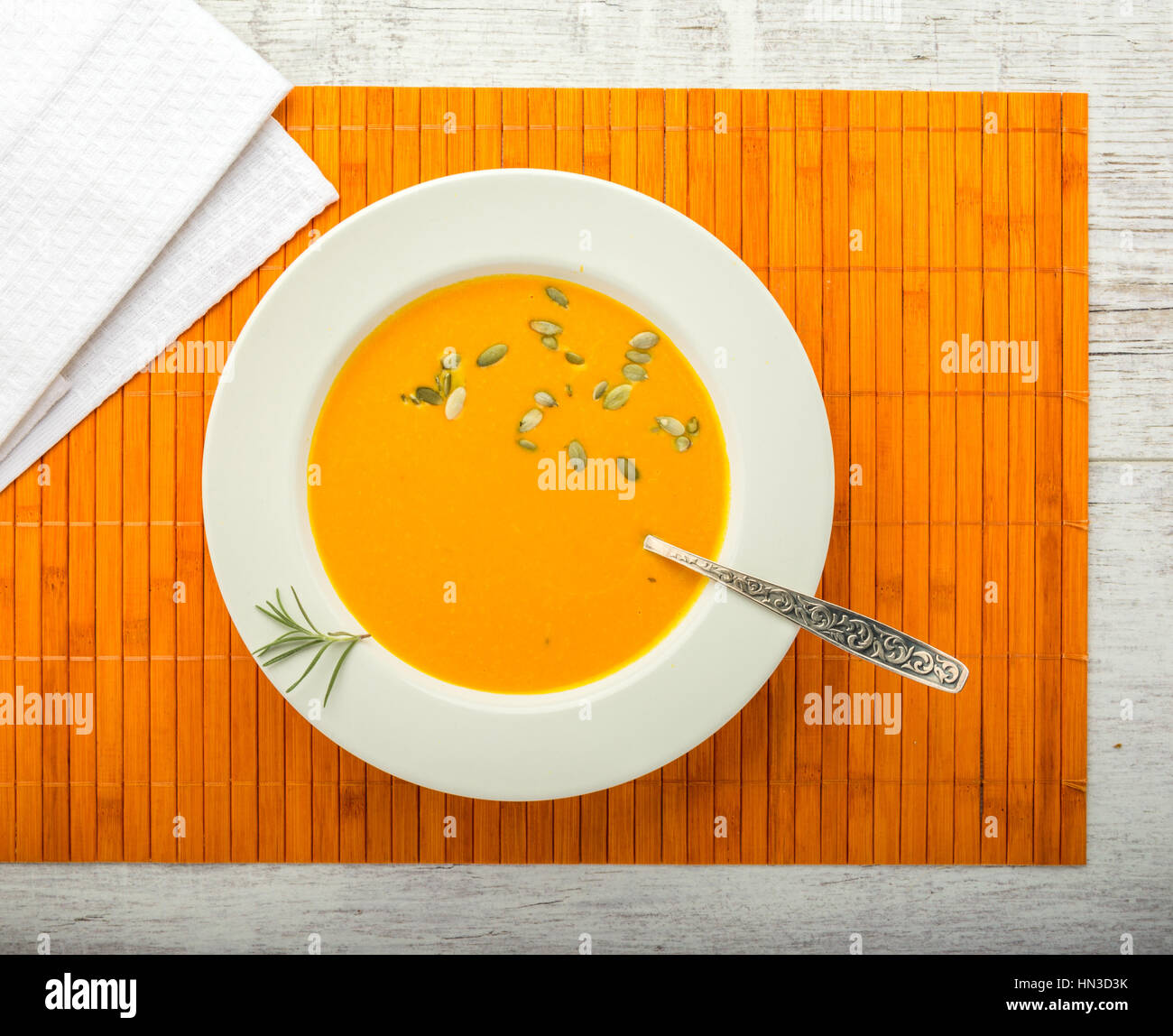 pumpkin cream soup with pumpkin seeds in a white plate with a spoon on a orange napkin closeup Stock Photo