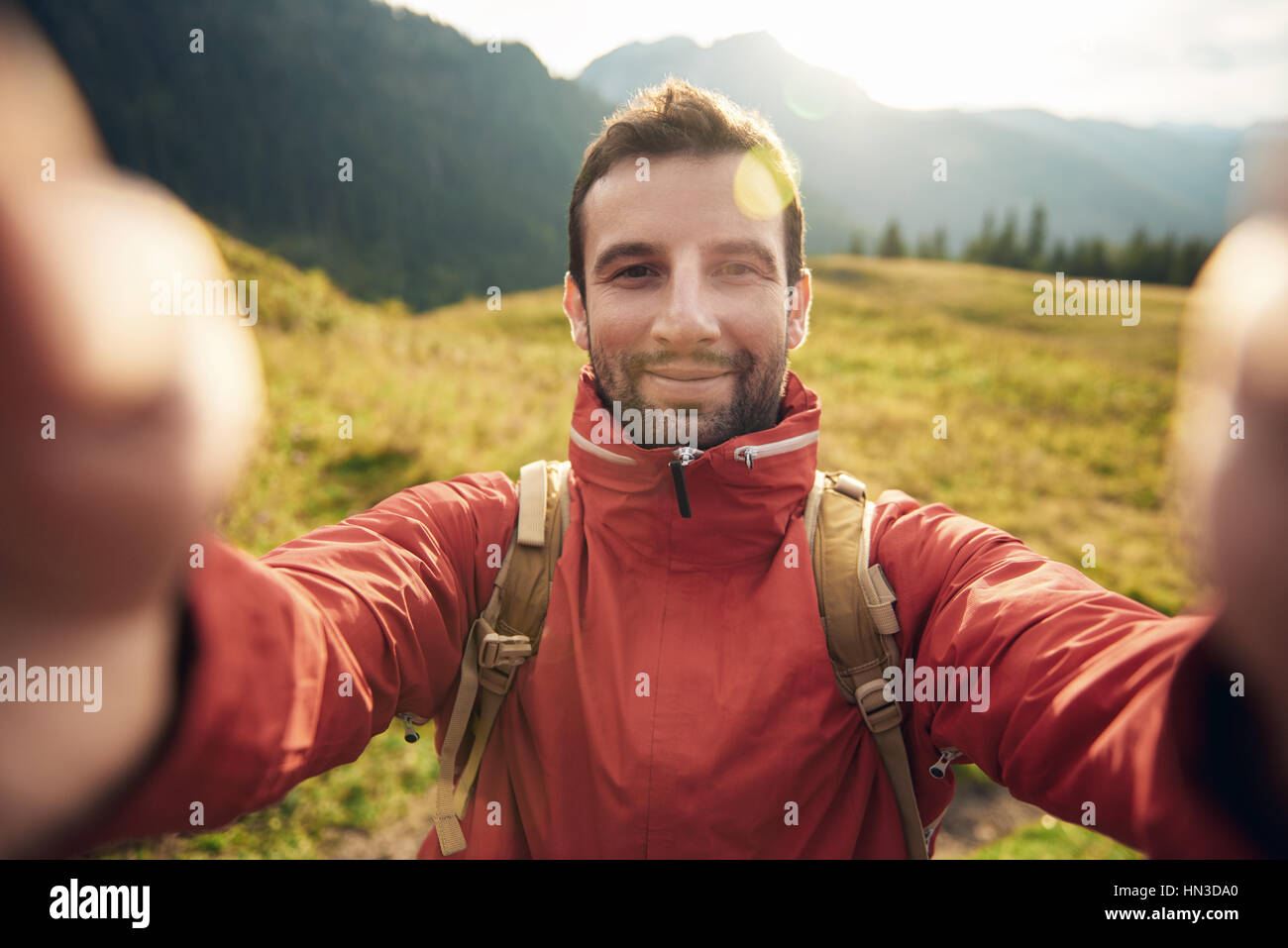 Young man in hiking gear standing outside taking a selfie with mountains behind him while out trekking in the wilderness Stock Photo
