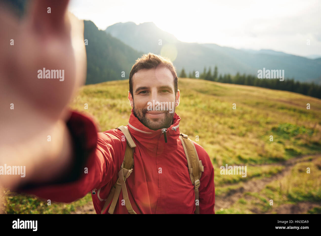 Young man in hiking gear standing outside taking a selfie with ...