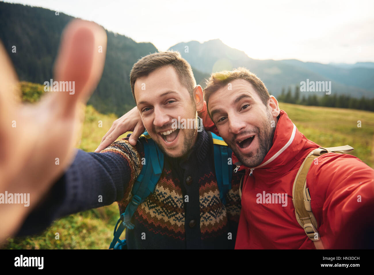 Two smiling young men in hiking gear standing outside taking a selfie ...