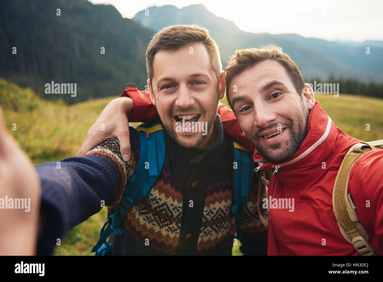 Two smiling young men in hiking gear standing outside taking a selfie ...