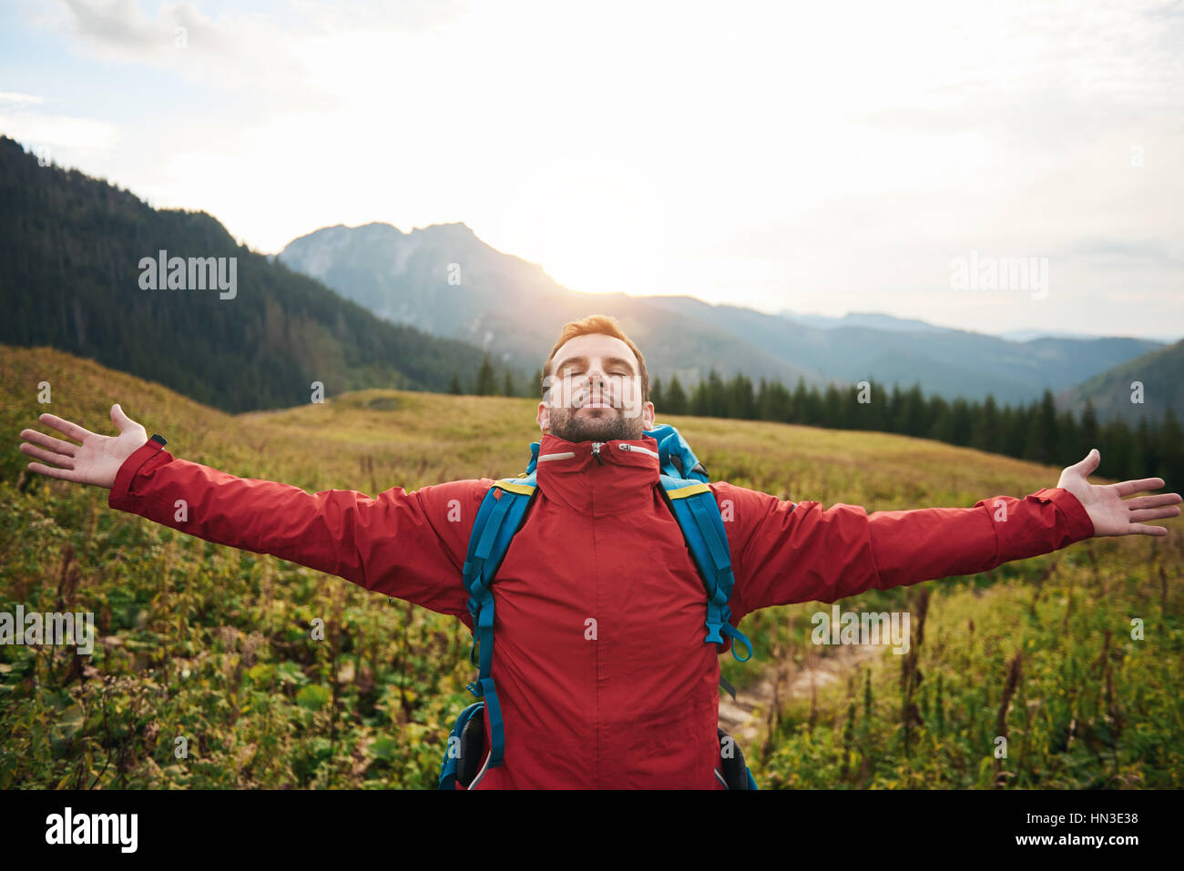 Young man in hiking gear with his arms raised to the sky embracing the ...
