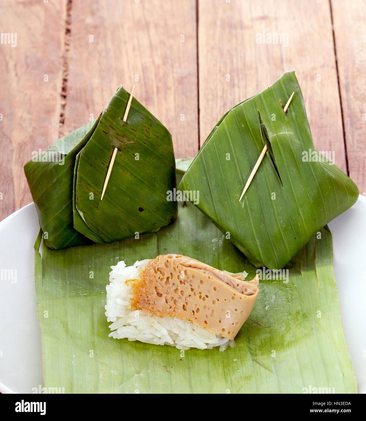 Thai Dessert - Sticky Rice with Egg Custard warpped by banana leaf on white dish Stock Photo