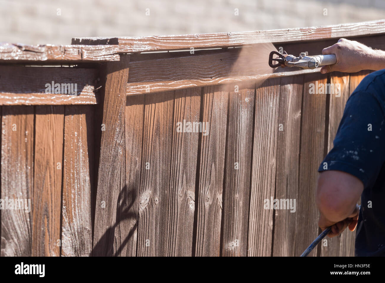 Professional Painter Spraying House Yard Fence with Wood Stain Stock