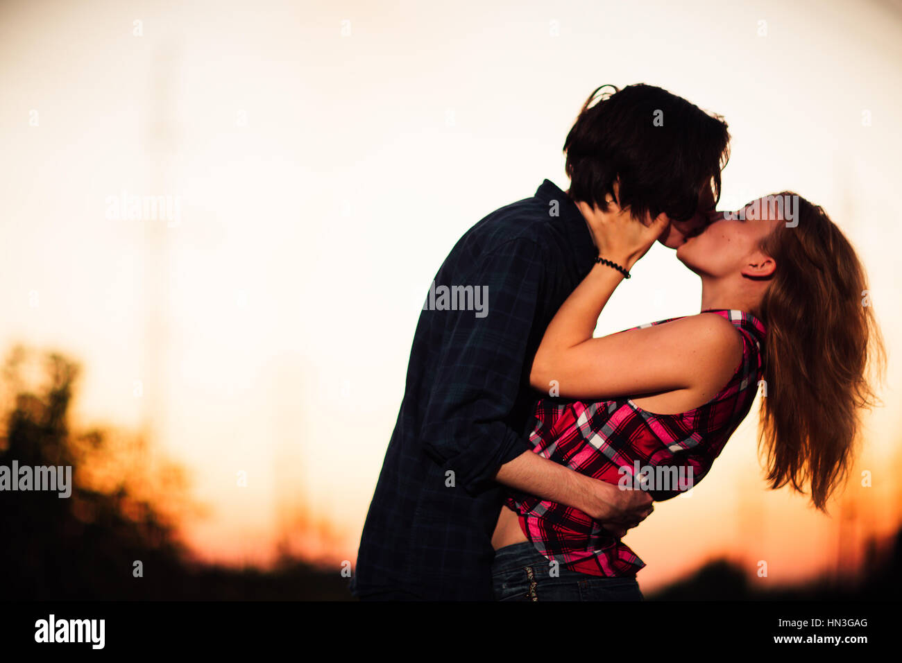 guy and the girl are standing kissing in the sunset background Stock Photo 