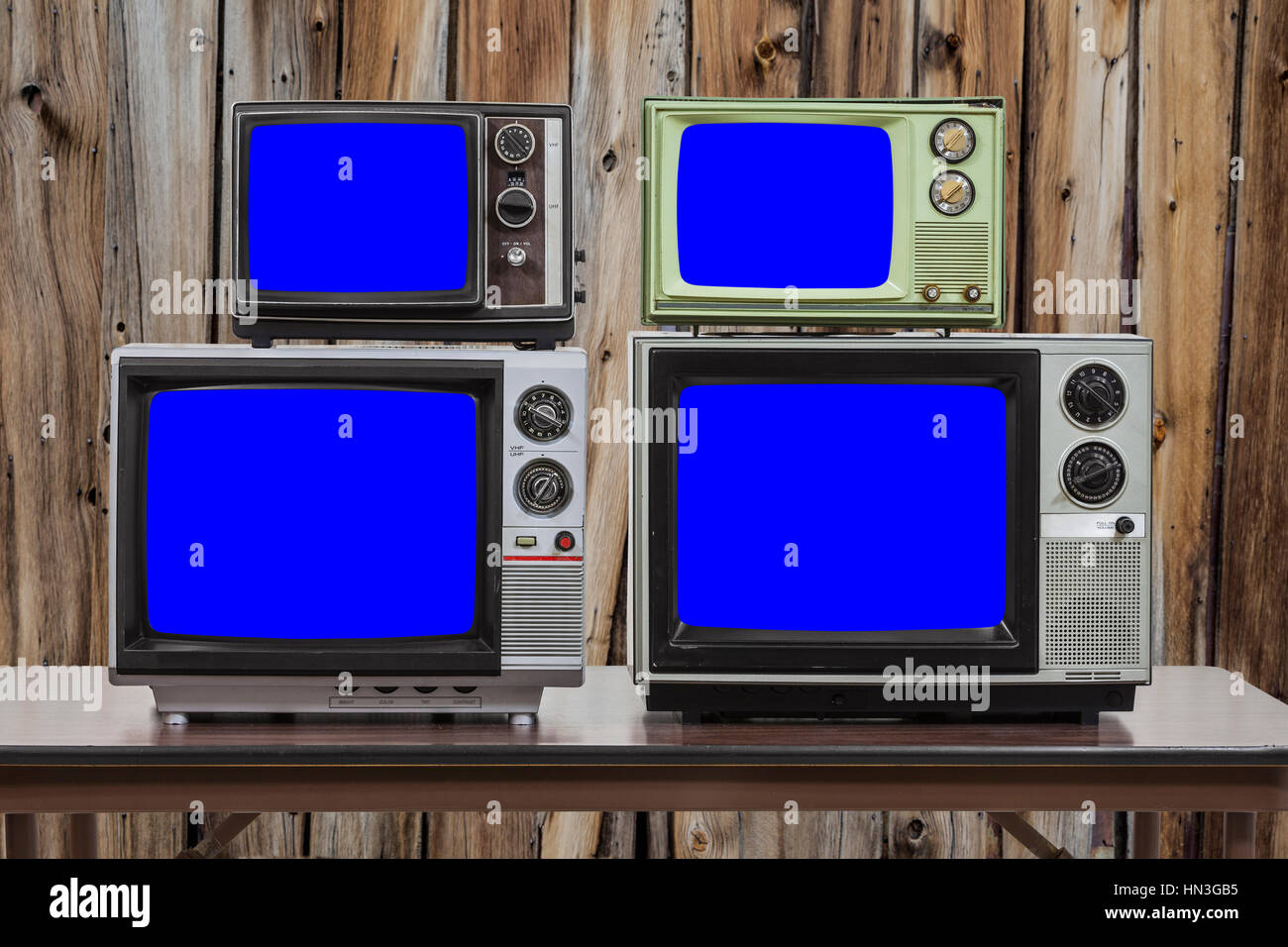 Four vintage televisions with old wood wall and chroma key blue screens. Stock Photo