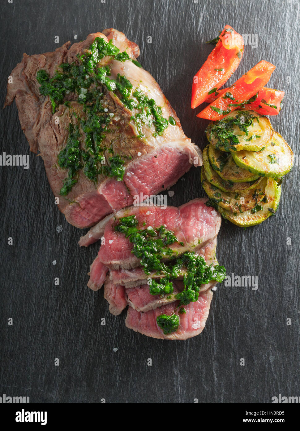 Roast Beef dinner with roasted zucchini, pepper and salsa verde on a stone plate Stock Photo