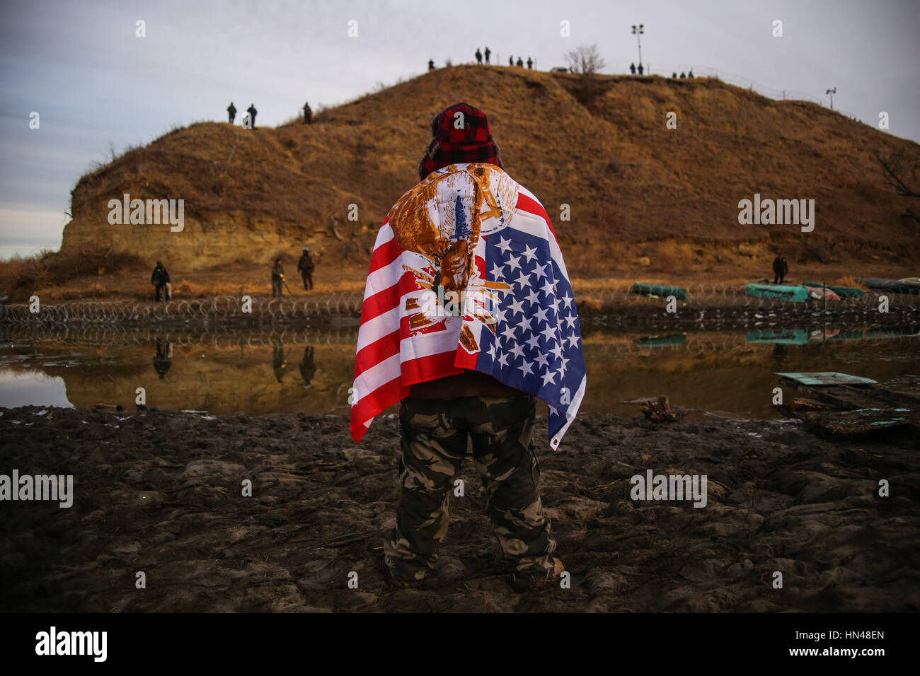 Cannon Ball, North Dakota, USA. 25th Nov, 2016. ANDREW WAUPEKENAY of the Menominee Indian Tribe of Wisconsin stands as he faces authorities on the other side of the Cantapeta Creek which runs into the Missouri River after barbed wire was placed along the shore near the Oceti Sakowin Camp on Army Corps of Engineers land bordering the Standing Rock Indian Reservation in Cannon Ball, North Dakota. Credit: Joel Angel Juarez/ZUMA Wire/Alamy Live News Stock Photo