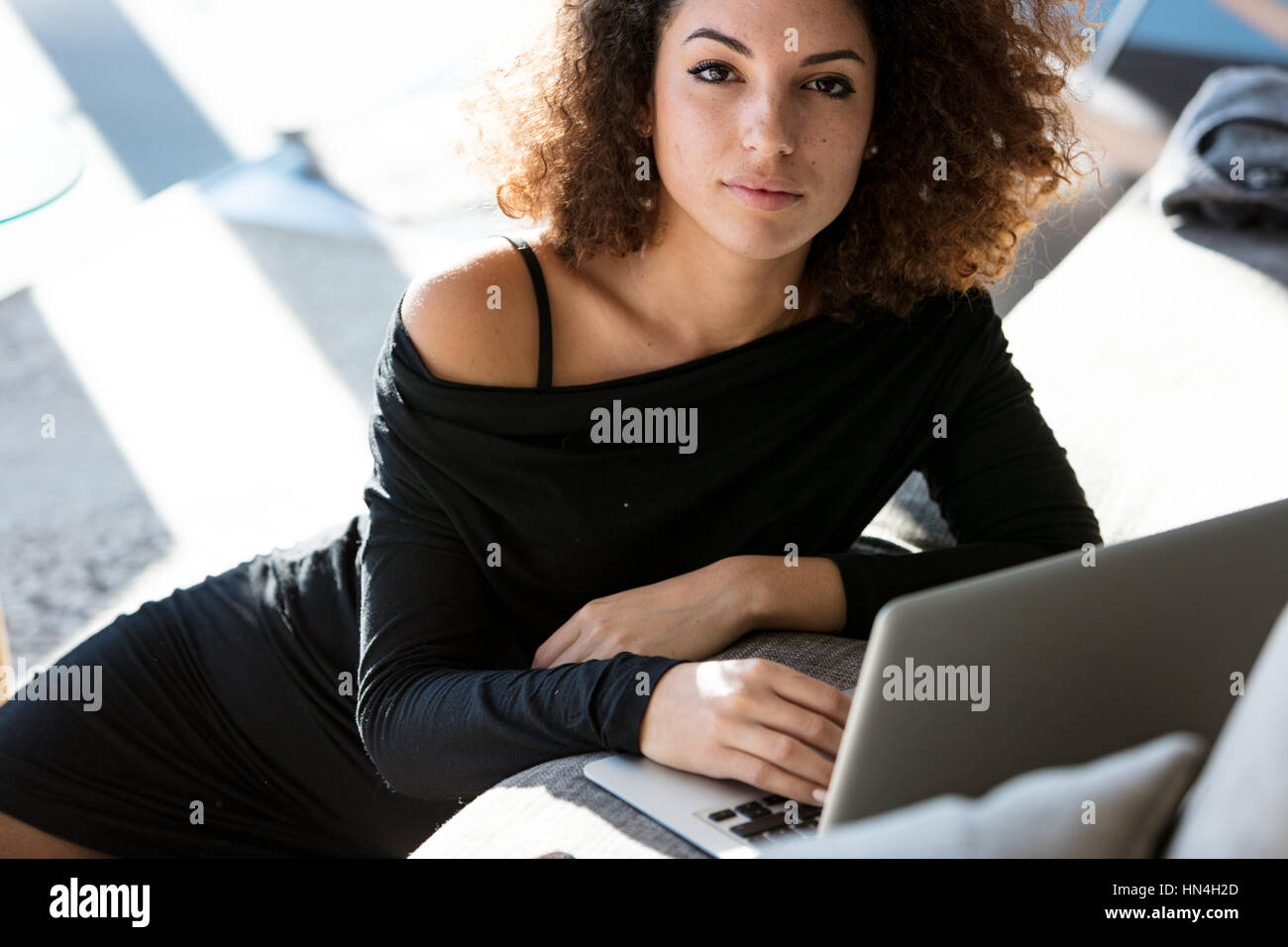 Serious young woman looking attentively at the camera with a calm expression as though waiting for something while working on a laptop Stock Photo