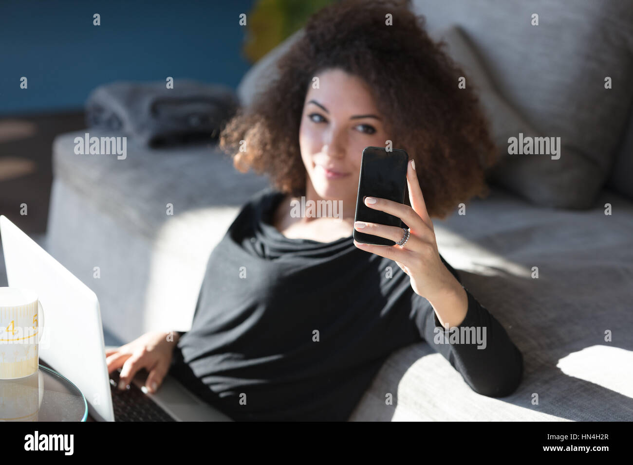 Attractive young woman relaxing on a couch with her laptop taking her ...