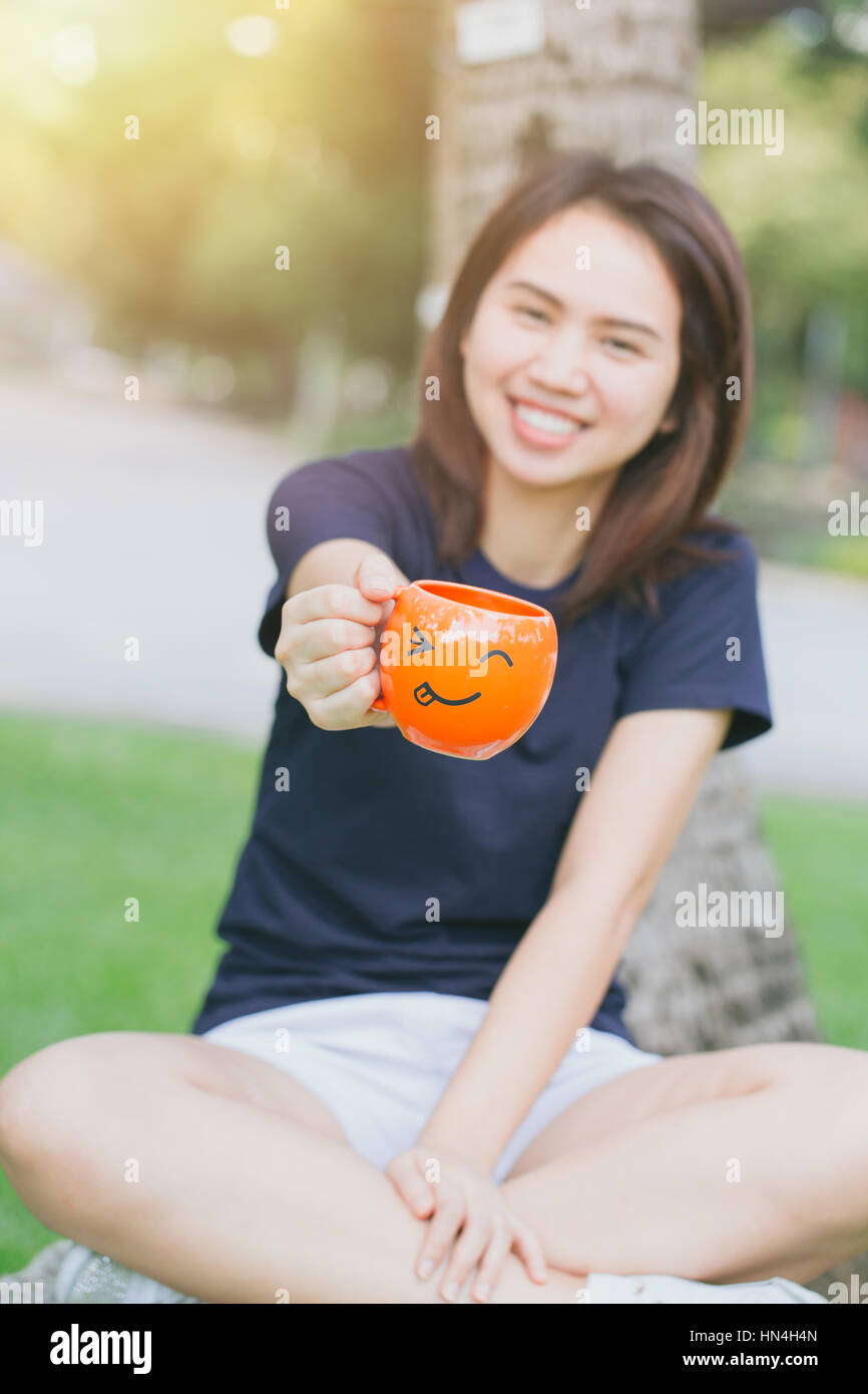 happy drink coffee concept with copy space, Asian girl teen working women adult handle smile mug in the green park. Stock Photo