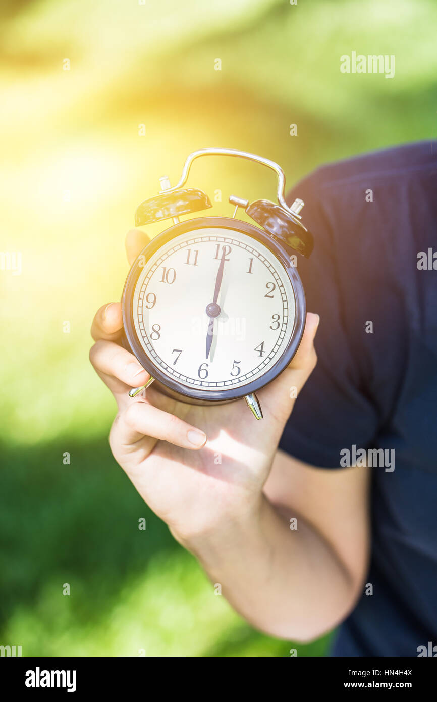 6 o'clock morning with hand hold the clock in the Clock park green garden with space for text. Stock Photo