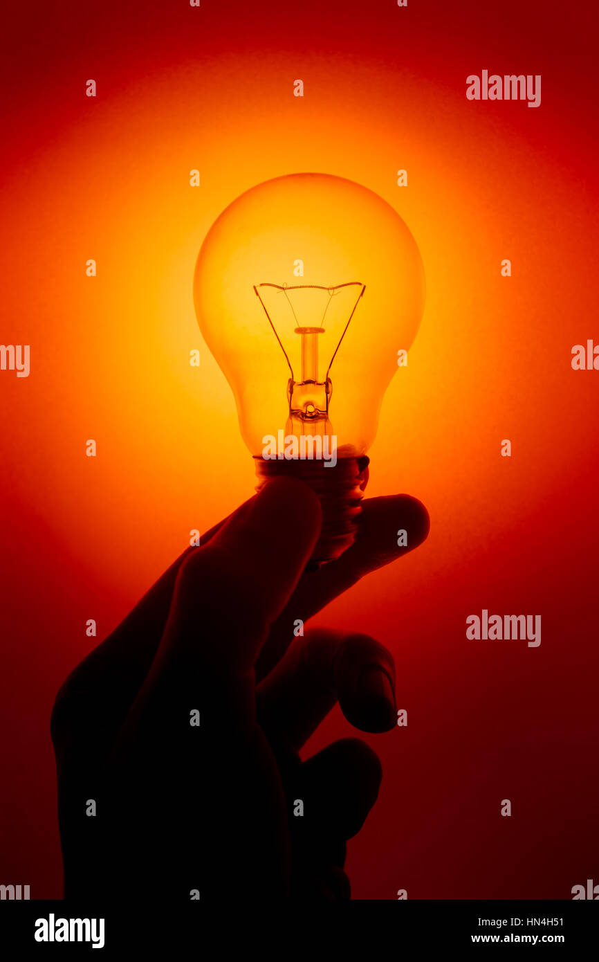 light bulb, silhouette hand hold Clear Glass Tungsten lighting bulb or Twisted Candle bulb on red color background. Stock Photo