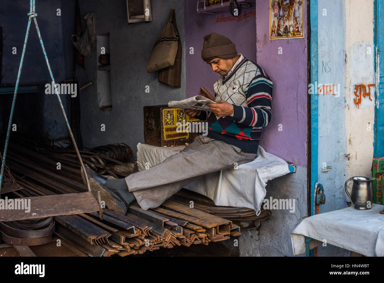 Indian man reading a newsapaper in his metal girder shop, Agra Stock Photo