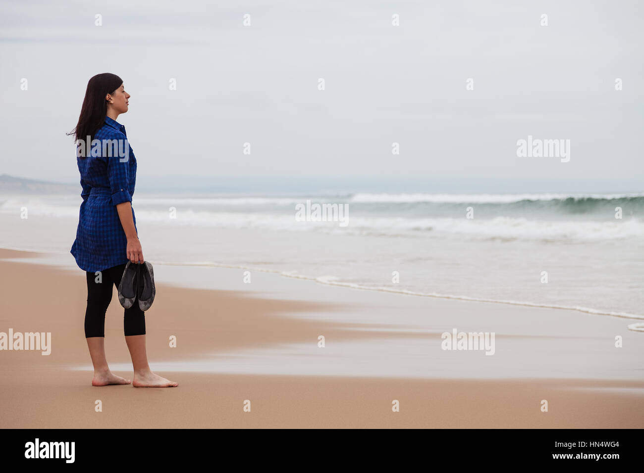 Lonely and depressed woman watching the sea in a deserted beach on an Autumn day / woman beach alone lonely sad sadness depressed looking watching sea Stock Photo