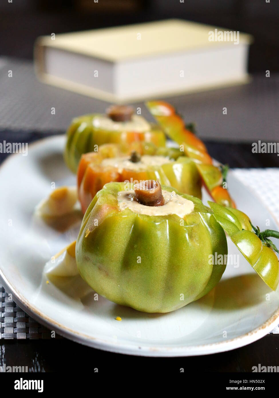 Stuffed green tomatoes in a white platter with eggs and a book in bokeh background - Still life objects and food series Stock Photo