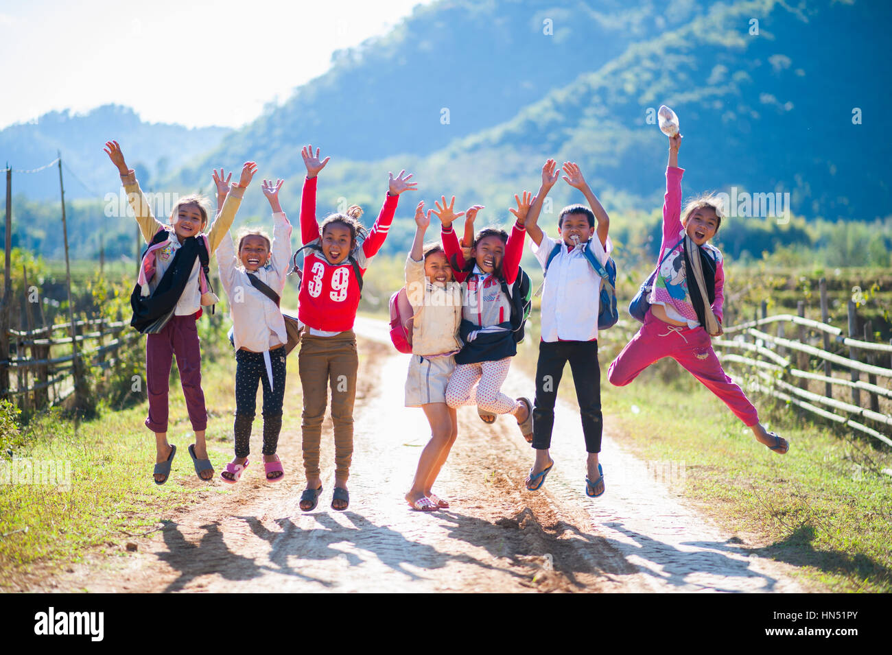 Always smiling and playful kids jumping in the air on a country road in Laos. Stock Photo