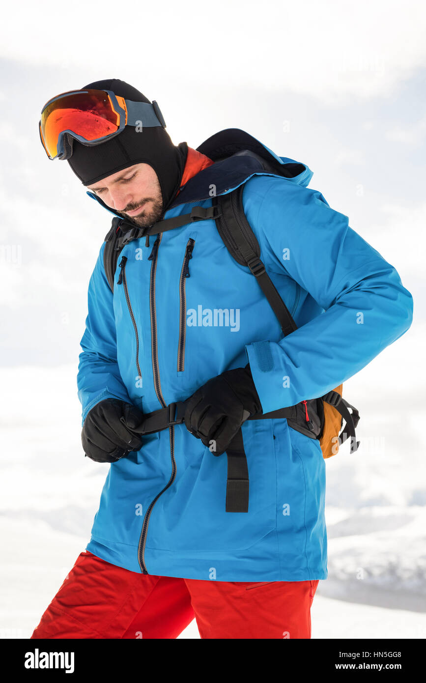 Skier tightening his backpack belt while getting ready for skiing Stock