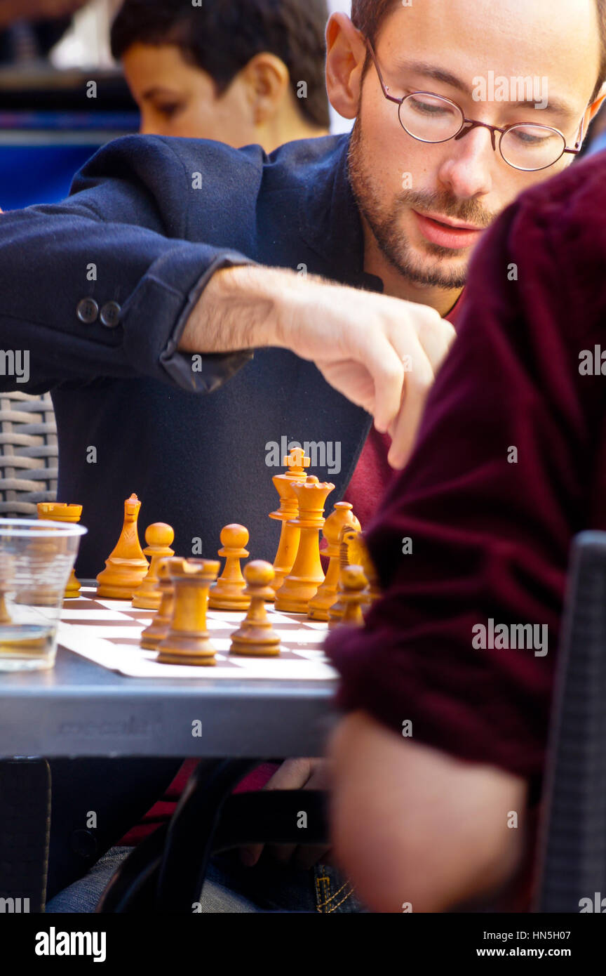 A young bearded man in glasses playing chess at an outdoor restaurant table, Toulouse, Haute-Garonne, Occitanie, France Stock Photo