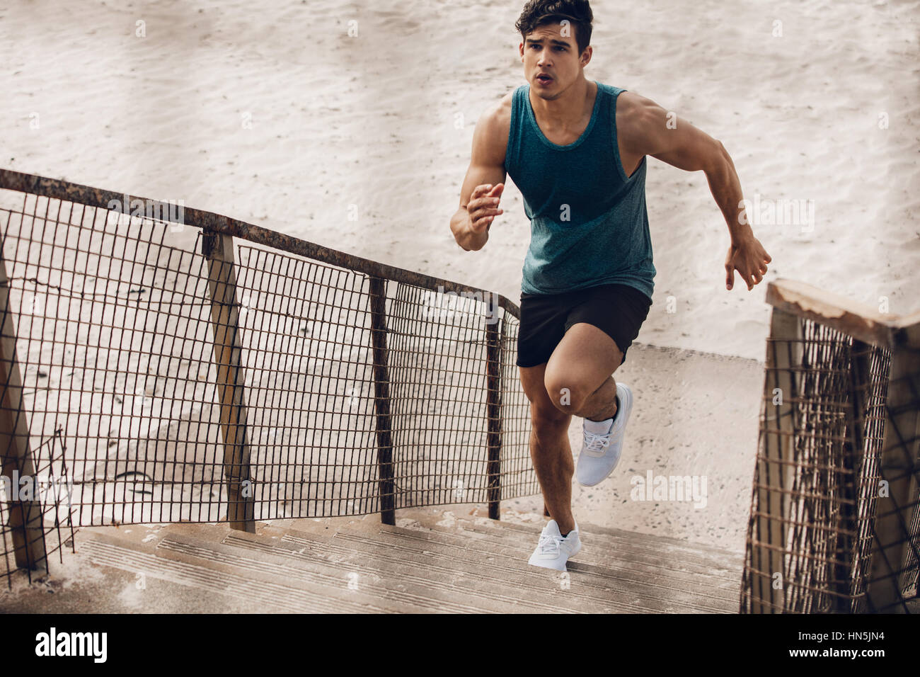 Fitness man running up the steps on beach. Muscular young male runner working out on steps on sea shore. Stock Photo