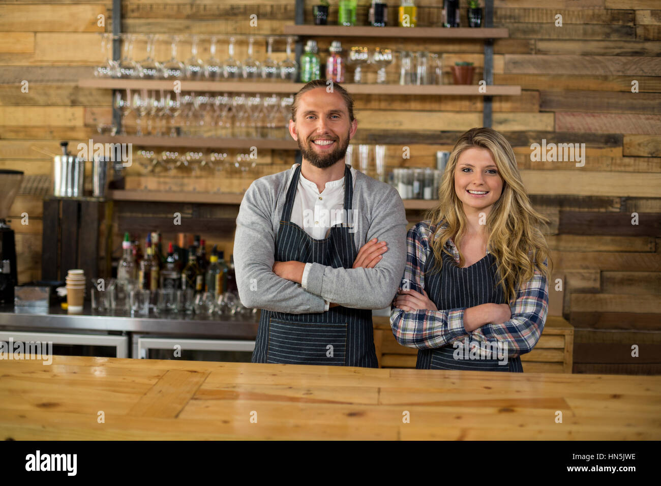 Portrait of smiling waiter and waitress standing with arms crossed at ...