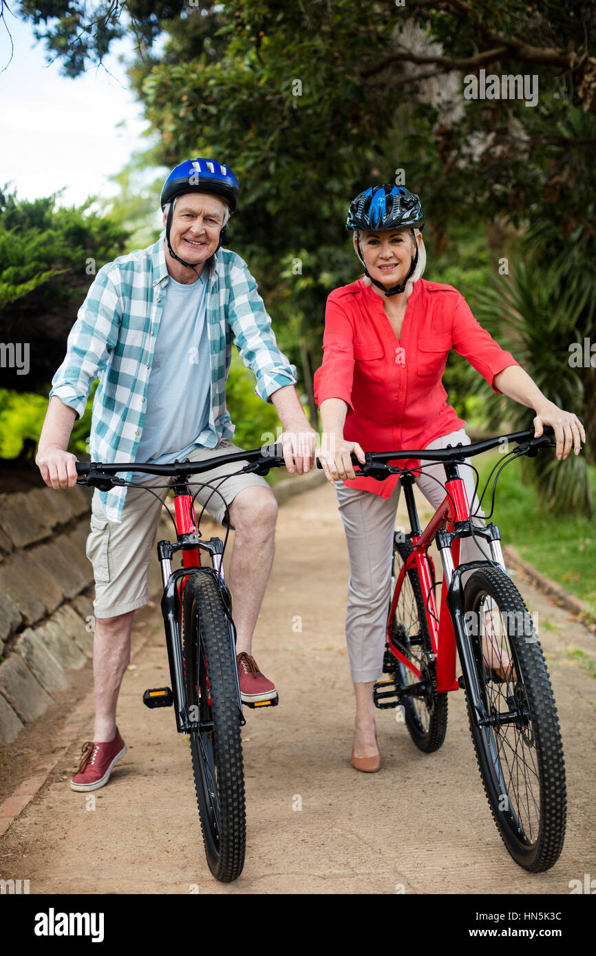 Portrait of senior couple standing with bicycle in park on a sunny day Stock Photo