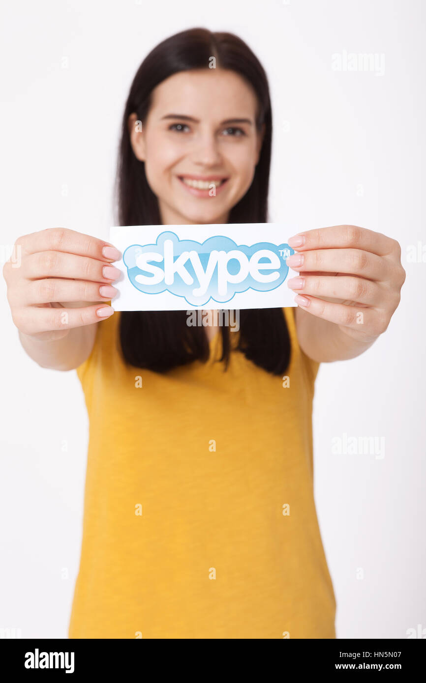 KIEV, UKRAINE - August 22, 2016: Woman hands holding Skype logotype printed on paper on grey background. Skype is a telecommunications application software developed by Microsoft. Stock Photo
