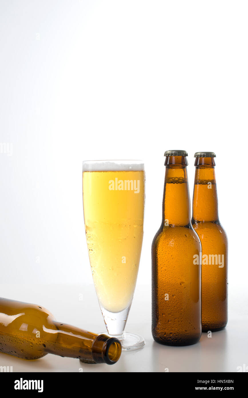 A glass of beer with empty and full bottles on each side set against a white background. Stock Photo