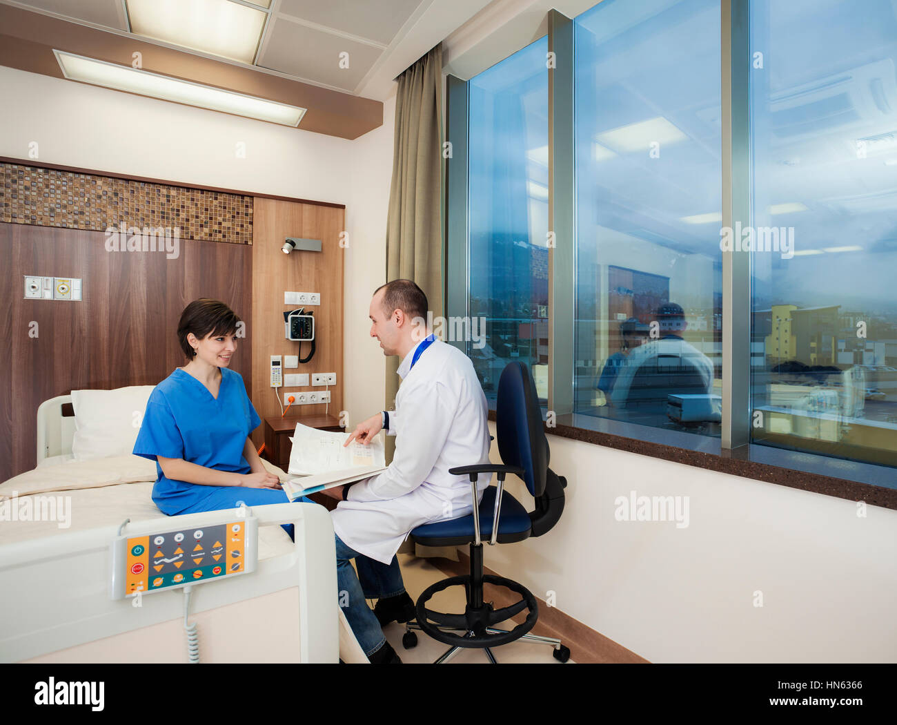 A doctor is bringing good news to a young female patient in modern hospital room. Stock Photo