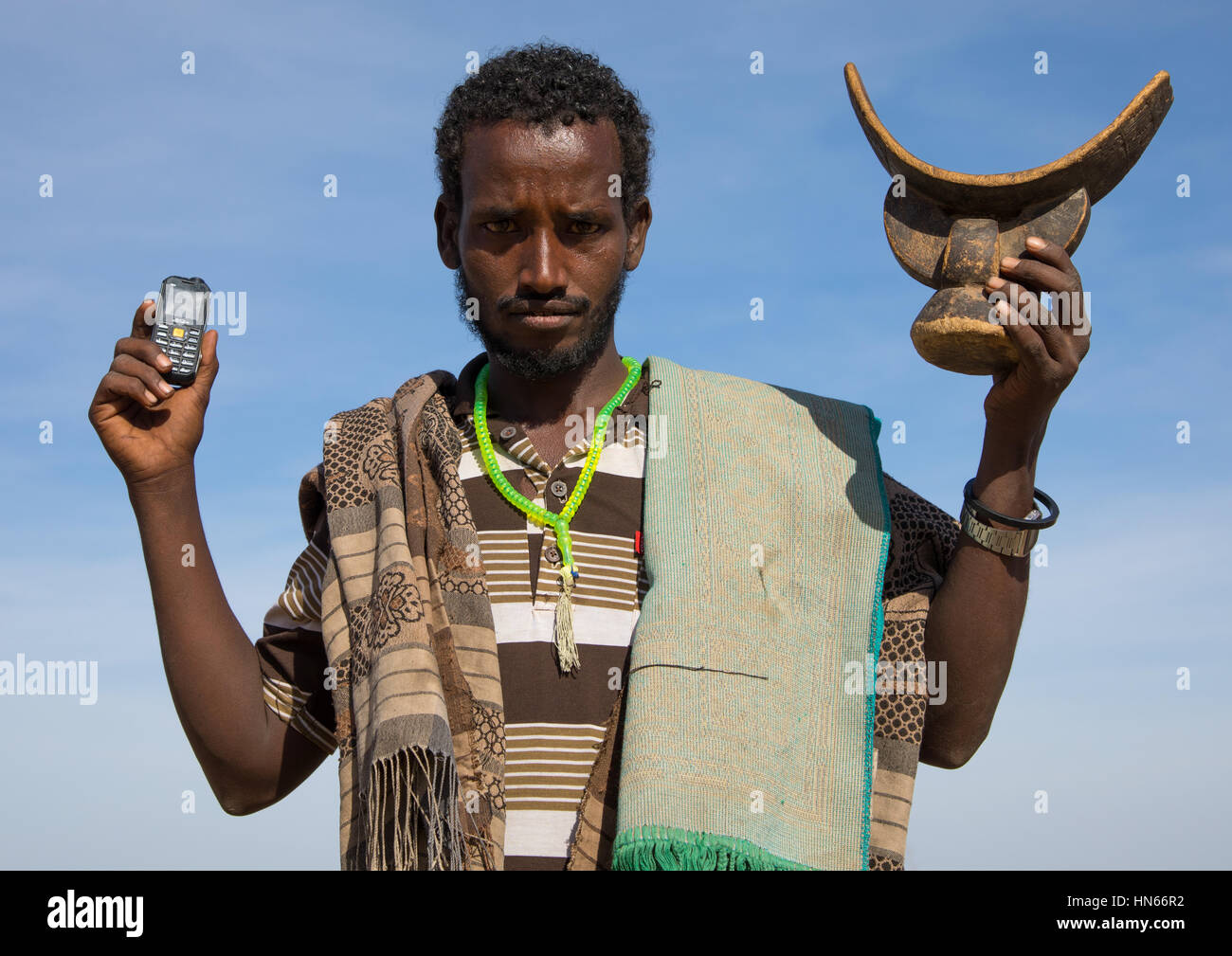 Issa tribe man holding a mobile phone and a wooden pillow, Afar region, Yangudi Rassa National Park, Ethiopia Stock Photo