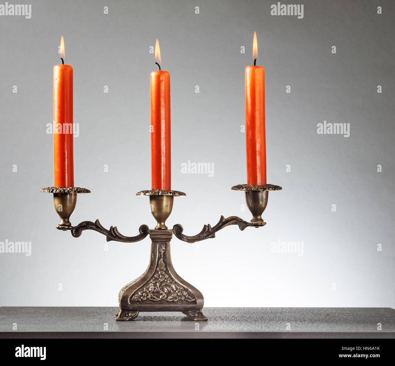 Antique bronze candlestick with three burning orange candles on gray background Stock Photo