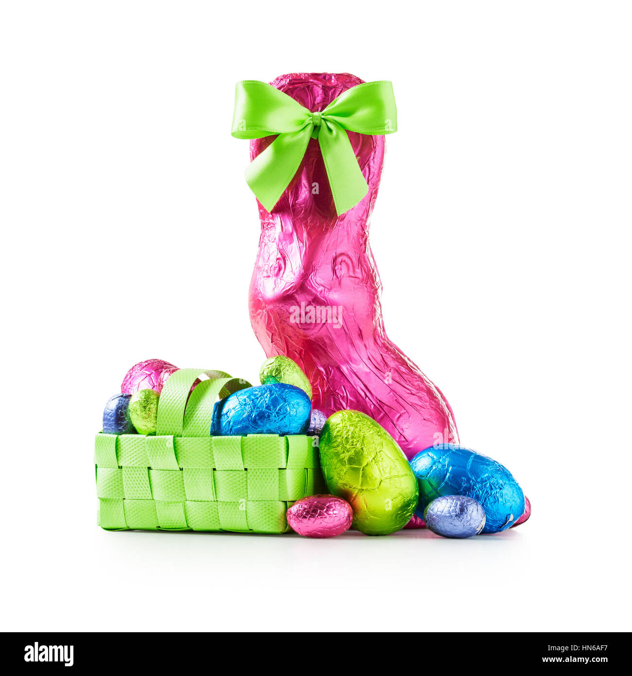 Chocolate easter eggs in basket, rabbit with bow wrapped in pink foil and colorful candies isolated on white background clipping path included Stock Photo