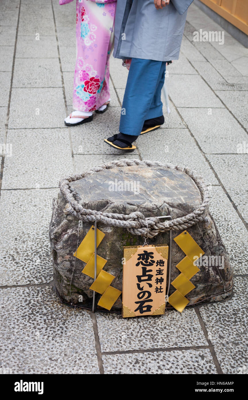 KYOTO, JAPAN - MARCH 24, 2012 : A 'love stone' at the Jishu Shrine with traditionally dressed couple in the background. Finding your way between stone Stock Photo