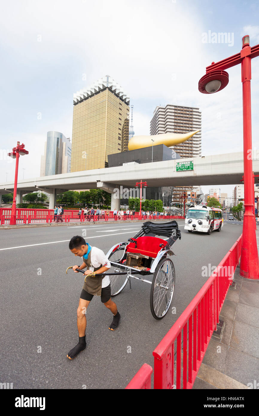 Tokyo, Japan - May 26, 2012: A man pulls an empty rickshaw across the Azuma bridge in Tokyo's Asakusa district with the gold coloured Asahi buildings  Stock Photo