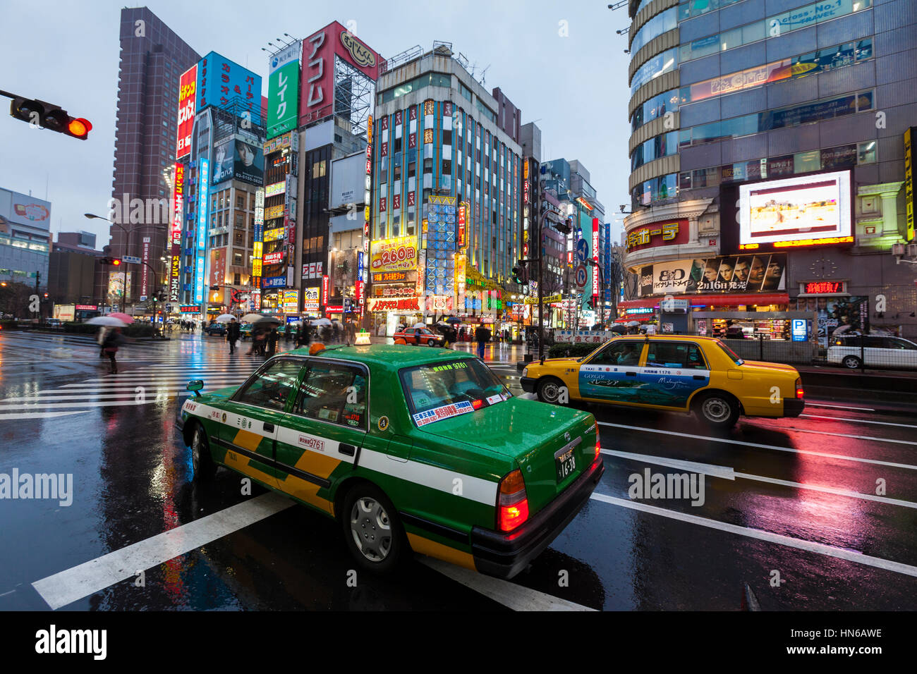 Tokyo, Japan - March 2, 2012: On a rainy evening, two Tokyo taxis wait at a road junction on Yasukuni Dori in Shinjuku, with colourfully lit buildings Stock Photo