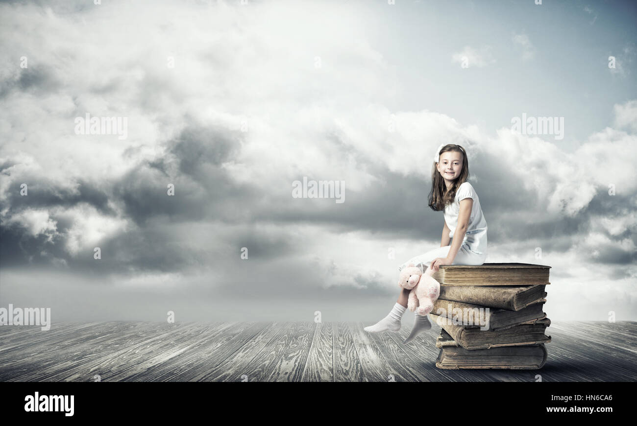 Little cute girl sitting on pile of books with bear toy in hand Stock ...