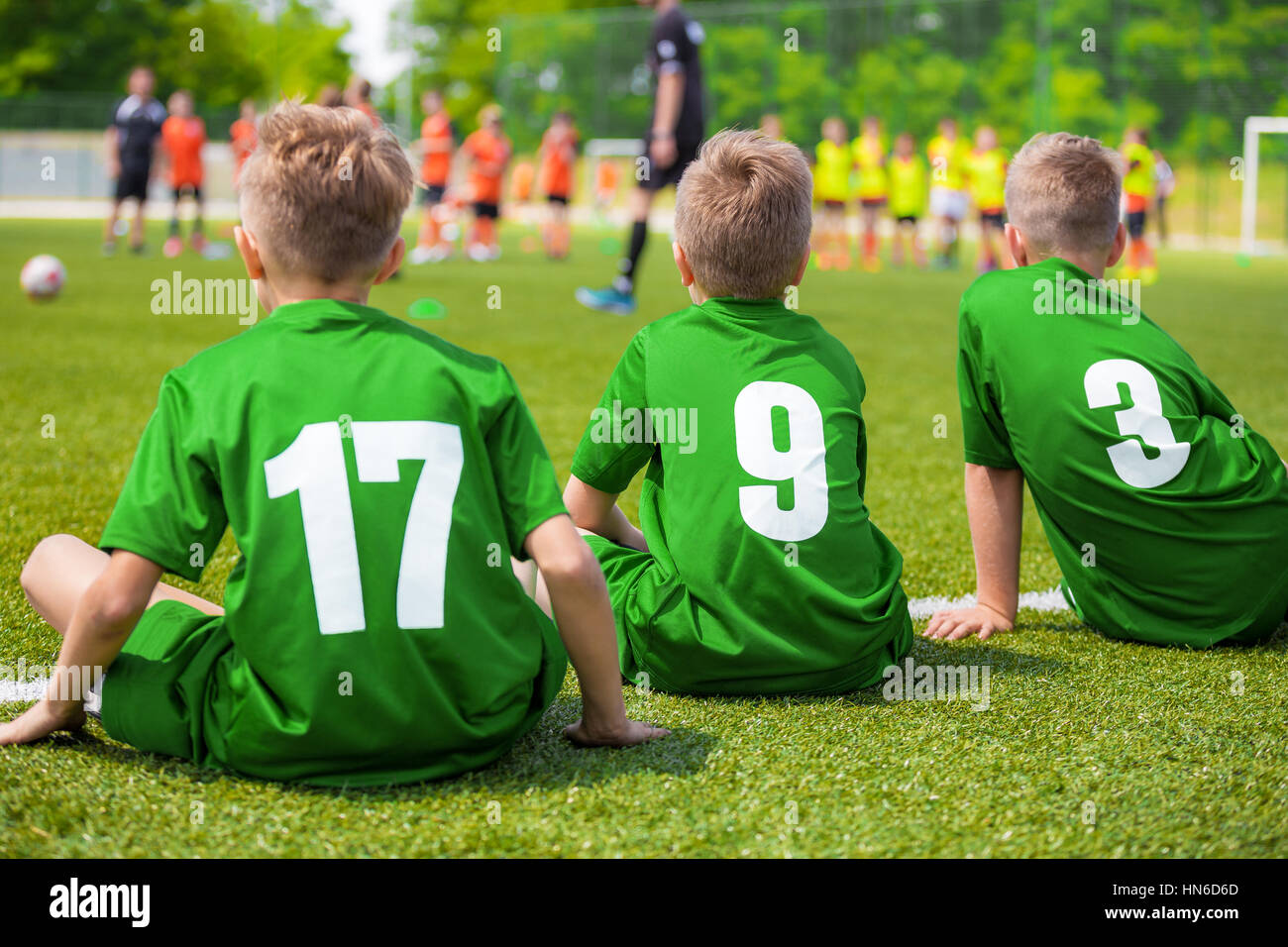 Kids Soccer Players Sitting on the Pitch. Young Boys of Football Team Sitting on Green Grass. Stock Photo